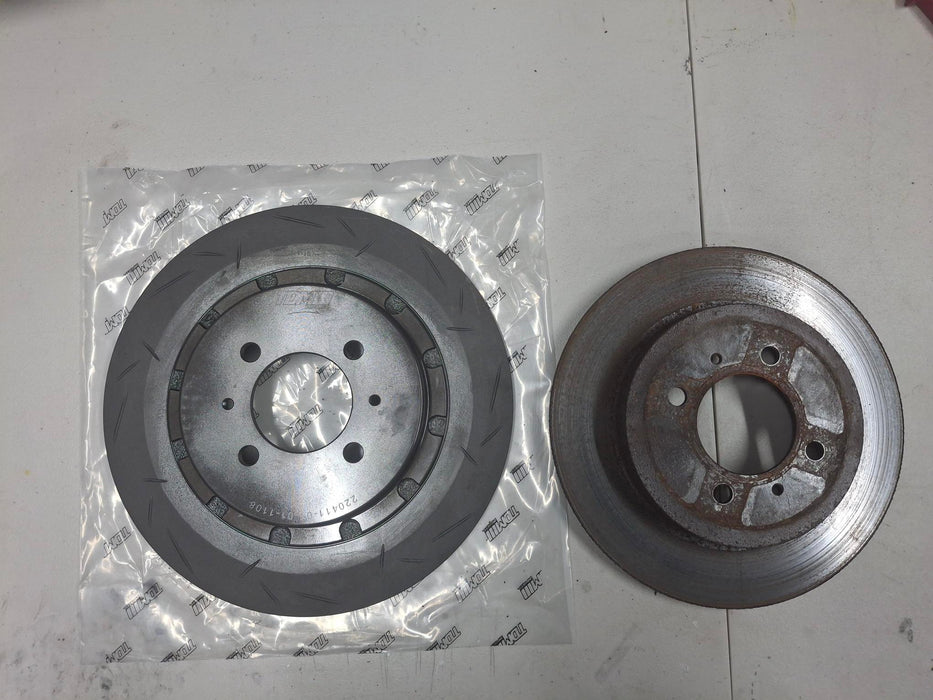 Two metal disc brake rotors on a white surface, one in a clear plastic bag.